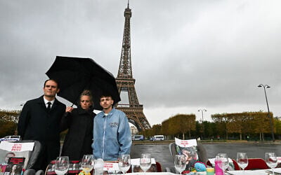 (De gauche à droite) Yonathan Arfi, président du Conseil représentatif des institutions juives de France (CRIF), Keren Shem, mère de Mia Shem, retenue en otage, et son fils, posent devant la Tour Eiffel (en arrière-plan) et une table présentant des images d'otages pris par le Hamas, lors d'une conférence de presse pour appeler à leur libération, à Paris, le 9 novembre 2023. (Crédit : STEFANO RELLANDINI / AFP)