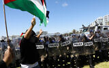 Des agents du Cape Town Metro Police Department (CTMPD) font la queue tandis qu'un homme agite un drapeau palestinien au Cap, le 12 novembre 2023, après que des partisans pro-israéliens ont été chassés par un groupe d'opposants. (Crédit : GIANLUIGI GUERCIA / AFP)