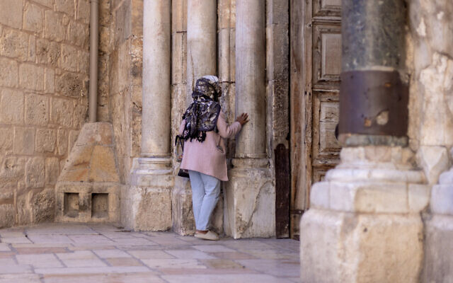Une femme prie à l'entrée de l'église du Saint-Sépulcre dans la vieille ville de Jérusalem, le 21 novembre 2023. (Crédit : Kenzo TRIBOUILLARD / AFP) Une femme prie à l'entrée de l'église du Saint-Sépulcre dans la vieille ville de Jérusalem, le 21 novembre 2023. (Crédit : Kenzo TRIBOUILLARD / AFP)