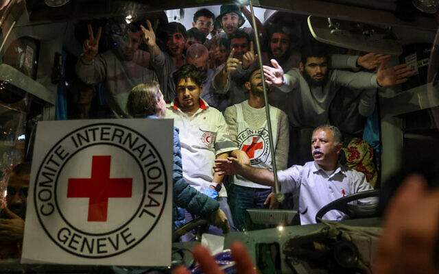 Un bus transportant du personnel de la Croix-Rouge et des prisonniers palestiniens libérés des prisons israéliennes en échange d'otages innocents libérés par le Hamas, traverse une foule de partisans brandissant des drapeaux palestiniens et du Hamas à Ramallah, en Cisjordanie, tôt le 26 novembre 2023. (Crédit : AHMAD GHARABLI / AFP)
