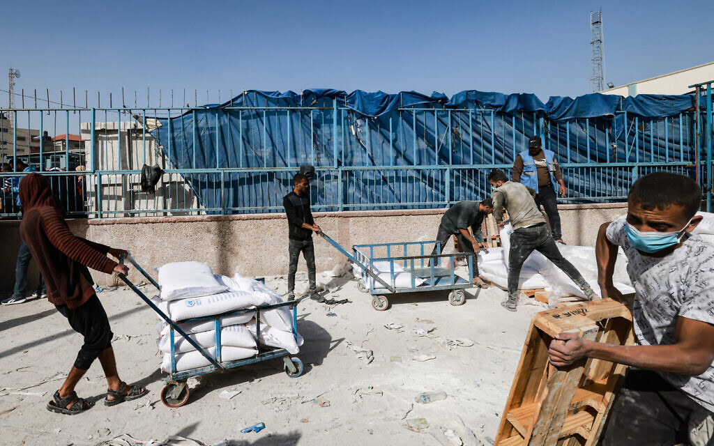 Des personnes tirant des chariots transportant des sacs d'aide humanitaire à distribuer, à Rafah, dans le sud de la bande de Gaza, le 26 novembre 2023 (Crédit : Mohammed Abed/AFP)