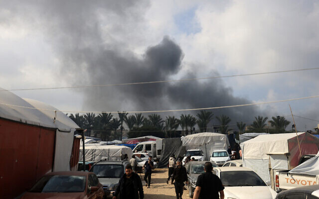 Des personnes marchant à l'intérieur d'un refuge temporaire pour personnes déplacées alors que de la fumée s'élève lors d'une frappe israélienne à Khan Yunis, dans le sud de la bande de Gaza, le 1er décembre 2023. (Crédit : Mahmud Hams/AFP) Des personnes marchant à l'intérieur d'un refuge temporaire pour personnes déplacées alors que de la fumée s'élève lors d'une frappe israélienne à Khan Yunis, dans le sud de la bande de Gaza, le 1er décembre 2023. (Crédit : Mahmud Hams/AFP)