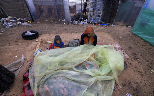 De jeunes Palestiniens sont assis, dehors, sur des matelas recouverts de plastique dans un camp de déplacés à Rafah, dans le sud de la bande de Gaza, le 13 décembre 2023, lors de la guerre entre Israël et le Hamas. (Crédit : Mahmoud HAMS / AFP)