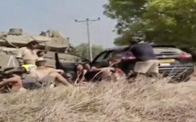 Des festivaliers s'abritent derrière un char, avec l'un des frères Sharabi, debout avec un casque à droite, en tentant de repousser les terroristes, le 7 octobre 2023 (Capture d'écran via Channel 12 utilisée conformément à l'article 27a de la loi sur les droits d'auteur)