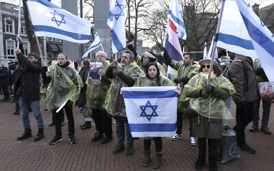 Des manifestants brandissqnt des drapeaux israéliens et néerlandais, et tenant des photos des otages enlevés lors de l'attaque transfrontalière du Hamas en Israël le 7 octobre, lors d'une manifestation devant la Cour internationale de justice, à La Haye, aux Pays-Bas, le 11 janvier 2024 (Crédit : Patrick Post/AP)