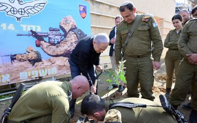 Le Premier ministre Benjamin Netanyahu, en noir, plantant un arbre sur une base militaire près de Gaza, le 25 janvier 2024. (Crédit : Amos Ben Gershom/GPO)