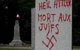 Illustration : Un graffiti en allemand et en français indiquant "Heil Hitler, mort aux Juifs" et avec une croix gammée, sur un monument à la mémoire de 55 personnes exécutées à cet endroit par les nazis en 1944 pendant la Seconde Guerre mondiale, à Ploeuc-L'Hermitage, dans l'ouest de la France, le 17 juillet 2023. (Crédit : Damien Meyer/AFP)