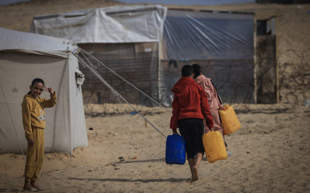 Des Palestiniens déplacés transportent de l'eau dans un camp de fortune à la frontière égyptienne, à l'ouest de Rafah, dans le sud de la bande de Gaza, le 14 janvier 2024. (Crédit : AFP)