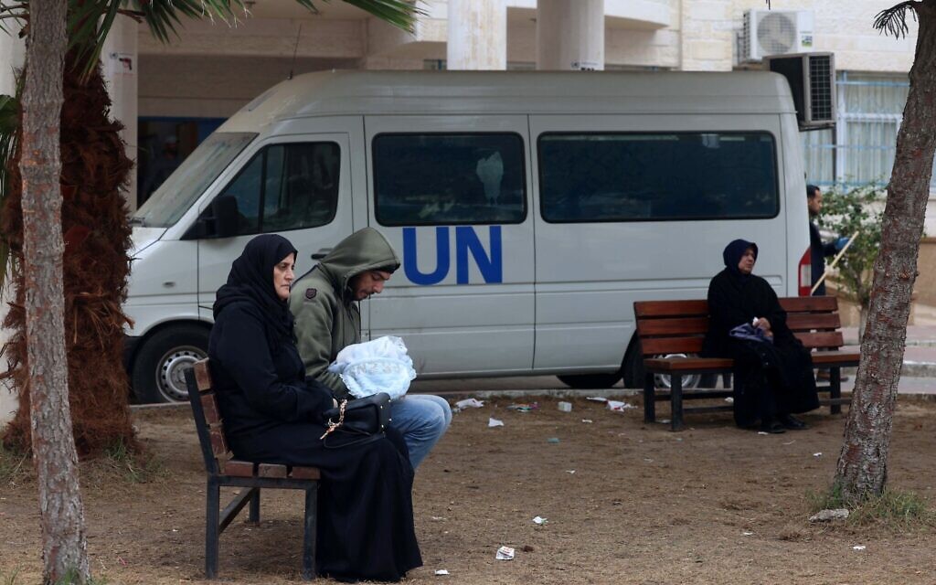 Des Palestiniens déplacés assis sur des bancs alors qu'ils attendent aux abords d'un dispensaire de l'UNRWA, agence de l'ONU chargée des réfugiés palestiniens, à Rafah, dans le sud de la bande de Gaza, le 28 janvier 2024. (Crédit :  AFP)