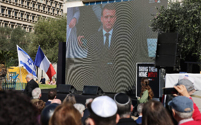 Des personnes regardent sur un grand écran la retransmission de l'hommage rendu par la France aux victimes françaises de l'attaque du 7 octobre du Hamas contre Israël, en présence du président Emmanuel Macron (à l'écran), devant le musée d'art de Tel Aviv, désormais appelé de manière informelle la "Place des otages", le 7 février 2024. (Crédit : AHMAD GHARABLI / AFP)