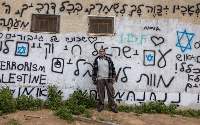 Shuki Yossef, 63 ans, pose à côté d'un graffiti en hébreu et en anglais portant des slogans contre l'attaque du 7 octobre par des combattants du Hamas, à Ofakim, une ville du sud d'Israël, à environ 25 kilomètres de la bande de Gaza, le 6 février 2024. (Crédit : Menahem Kahana / AFP)