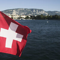 Le drapeau national suisse devant le lac Léman, à Genève, le 13 juin 2021. (Crédit : Markus Schreiber/AP)