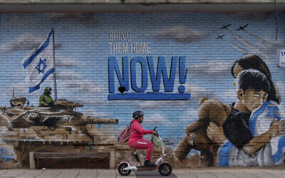 Une personne passe en scooter devant une fresque murale demandant le retour des otages enlevés lors de l'attaque transfrontalière du Hamas du 7 octobre en Israël, à Kfar Saba, en Israël, le lundi 26 février 2024. (Crédit : AP/Ohad Zwigenberg)