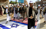 Des membres des Houthis soutenus par l'Iran au Yémen marchant sur des drapeaux israéliens et américains peints dans la rue à Sanaa lors d'un rassemblement de soutien aux Palestiniens dans le cadre de la guerre entre Israël et le groupe terroriste Hamas à Gaza, le 28 février 2024. (Crédit : Mohammed Huwais/AFP)