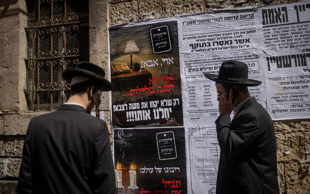 Des Juifs ultra-orthodoxes devant une affiche sur la loi sur la conscription de Tsahal dans le quartier ultra-orthodoxe de Mea Shearim, à Jérusalem, le 15 mars 2024. (Crédit : Chaim Goldberg/Flash90) Des Juifs ultra-orthodoxes devant une affiche sur la loi sur la conscription de Tsahal dans le quartier ultra-orthodoxe de Mea Shearim, à Jérusalem, le 15 mars 2024. (Crédit : Chaim Goldberg/Flash90)