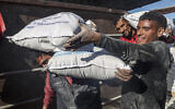 Des travailleurs déchargeant des sacs d'aide humanitaire entrés à Gaza par camion à travers le poste-fronière israélien de Kerem Shalom, à Rafah, dans le sud de la bande de Gaza, le 17 février 2024. (Crédit : Saïd Khatib/AFP)