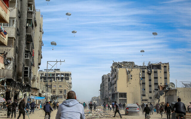Des Palestiniens courent le long d'une rue lors du largage par voie aérienne d'aides humanitaires sur Gaza City, le 1er mars 2024. (Crédit :AFP)