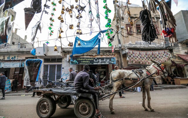 Un jeune garçon dans une cariole à âne devant un magasin vendant des lumières et des lanternes décoratives à  Deir al-Balah, dans le centre de Gaza, alors que les musulmans se préparent pour le mois sacré du ramadan, in central Gaza, as Muslims prepare for the holy fasting month of Ramadan on March 3, 2024. (AFP)