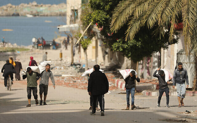 Des Palestiniens transportent des sacs de farine alors que l'aide humanitaire arrive dans la ville de Gaza le 6 mars 2024, dans le cadre du conflit actuel entre Israël et le Hamas. (Crédit : AFP) Des Palestiniens transportent des sacs de farine alors que l'aide humanitaire arrive dans la ville de Gaza le 6 mars 2024, dans le cadre du conflit actuel entre Israël et le Hamas. (Crédit : AFP)