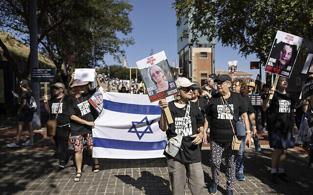 Des manifestants brandissant des pancartes et un drapeau israélien lors d'une manifestation organisée par le South African Jewish Board of Deputies à l'occasion de la Journée internationale des droits des femmes dénonçant le silence du gouvernement sud-africain sur les mauvais traitements infligés aux otages détenus par le Hamas, à Johannesburg, le 8 mars 2024. (Crédit : OLYMPIA DE MAISMONT/AFP)