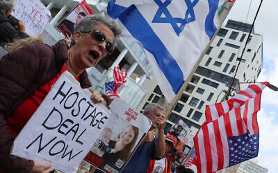 Des proches des otages et leurs soutiens brandissent des drapeaux et des panneaux appelant les États-Unis à intervenir pour les faire libérer lors d'un rassemblement à Tel Aviv, coïncidant avec la visite du secrétaire d'État américain dans le pays, le 22 mars 2024. (Crédit : Jack Guez/AFP)
