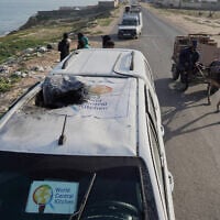 Des personnes se rassemblent autour de l’épave d’un véhicule de l’organisation humanitaire américaine World Central Kitchen, touché la veille par une frappe israélienne, à Deir al-Balah, dans le centre de la bande de Gaza, le 2 avril 2024. (Crédit : AFP)
