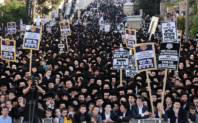Des hommes et des jeunes juifs ultra-orthodoxes brandissant des pancartes lors d'une manifestation contre la conscription dans l'armée israélienne devant un bureau de recrutement de l'armée, à Jérusalem, le 11 avril 2024. (Crédit : Menahem Kahana/AFP) Des hommes et des jeunes juifs ultra-orthodoxes brandissant des pancartes lors d'une manifestation contre la conscription dans l'armée israélienne devant un bureau de recrutement de l'armée, à Jérusalem, le 11 avril 2024. (Crédit : Menahem Kahana/AFP)