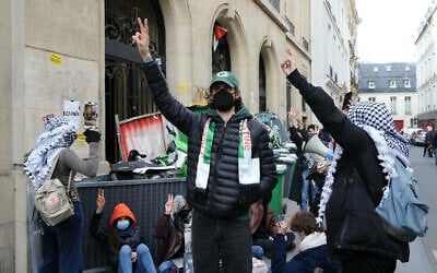 Des manifestants anti-Israël faisant le signe de la victoire lors de "l'occupation" d'un bâtiment de l'Institut d'études politiques (Sciences Po Paris) par des étudiants en soutien aux Palestiniens, avec une barricade bloquant son entrée, à Paris, le 26 avril 2024. (Crédit : Dimitar Dilkoff/AFP)