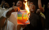 Des partisans du religieux chiite irakien Moqtada Sadr brûlant une affiche représentant un drapeau LGBTQ+ lors d'une manifestation, à Karbala, le 29 juin 2023. (Crédit : Mohammed Sawaf/AFP)