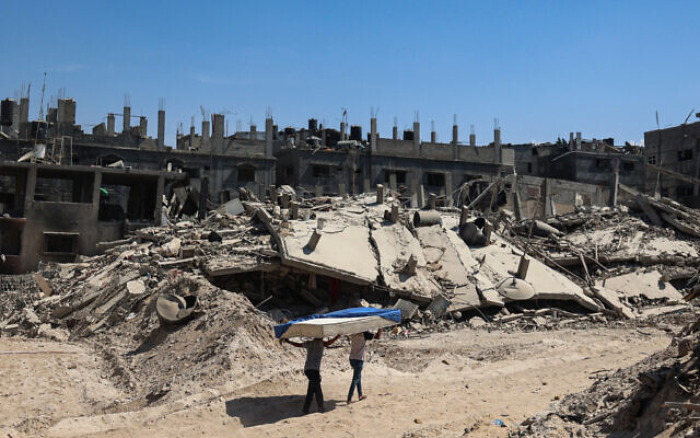 Des Palestiniens transportant un matelas sur un chemin, dans les décombres des immeubles de Khan Younès, le 7 avril 2024. (Crédit :  AFP)