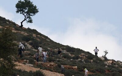 Des résidents d’implantations israéliens armés rassemblés sur une colline surplombant le village d'al-Mughayyir, non loin de de Ramallah, en Cisjordanie, le 13 avril 2024. (Crédit : Jaafar Ashtiyeh/AFP)