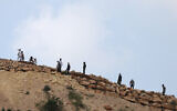 Des résidents d’implantations masqués rassemblés sur une colline surplombant le village de Mughayir, à proximité de Ramallah, en Cisjordanie, le 13 avril 2024. (Crédit : Jaafar Ashtiyeh/AFP)