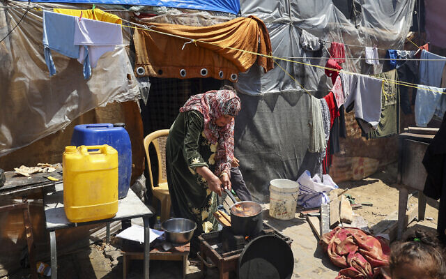 Une femme cuisinant à l'extérieur de son abri de fortune, dans un camp de déplacés palestiniens à Rafah, dans le sud de la bande de Gaza, le 14 avril 2024. (Crédit : AFP)