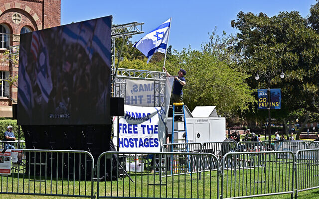 Un soutien d'Israël accroche un drapeau israélien à l'intérieur des barricades en métal qui entourent un campement pro-palestinien sur le campus de l'université de Californie-Los Angeles, l'UCLA, le 29 avril 2024. (Crédit : Frederic J. BROWN / AFP) Un soutien d'Israël accroche un drapeau israélien à l'intérieur des barricades en métal qui entourent un campement pro-palestinien sur le campus de l'université de Californie-Los Angeles, l'UCLA, le 29 avril 2024. (Crédit : Frederic J. BROWN / AFP)