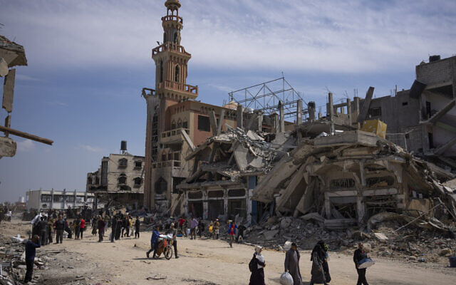 Les Palestiniens marchant à travers les destructions à Khan Younès après les batailles féroces entre Israël et le Hamas et le retrait des troupes israéliennes du sud de la bande de Gaza, le 8 avril 2024. (Crédit : Fatima Shbair/AP Photo)