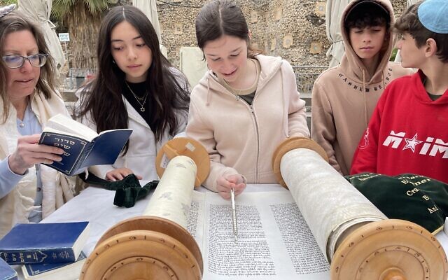 L'enseignante Jessica Lissy (à gauche) et ses élèves de la Hannah Senech Community Day School lisant un rouleau de la Torah, à Jérusalem, le 25 mars 2024. (Crédit : Autorisation)