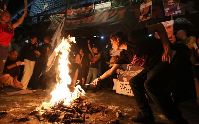 Une manifestante allumant une cigarette à partir du feu de joie allumé lors de la manifestation pour le retour des otages, rue Begin, à Tel Aviv, le 6 avril 2024. (Crédit : Roï Boshi/Mouvement de protestation pour la démocratie)