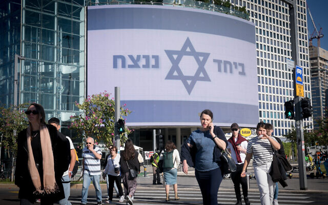 Des gens passent devant un grand panneau d'affichage indiquant "Ensemble, nous vaincrons" au centre commercial Azrieli à Tel Aviv, le 19 décembre 2023. (Crédit : Miriam Alster/Flash90)