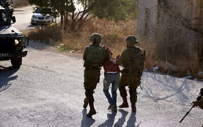 Illustration : Des soldats israéliens arrêtent un Palestinien lors d'une opération de recherche dans le village de Baita, en Cisjordanie, le 21 août 2023. (Crédit : Jaafar Ashtiyeh/AFP)