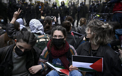 Des manifestants organisent un sit-in devant des policiers anti-émeutes français près de l'entrée d'un bâtiment de l'Institut d'études politiques (Sciences Po Paris) occupé par des étudiants, à Paris, le 26 avril 2024. (Crédit : JULIEN DE ROSA / AFP)