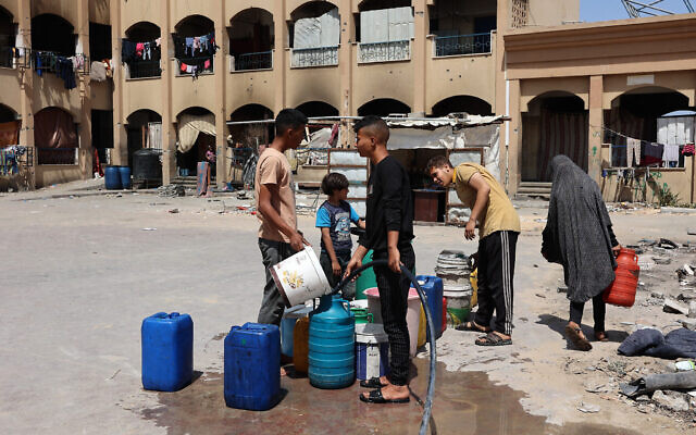 Des Palestiniens déplacés remplissant des jerrycans d'eau, dans une école utilisée comme abri temporaire, à Beit Lahiya dans le nord de la bande de Gaza, le 4 mai 2024 (Crédit : AFP)
