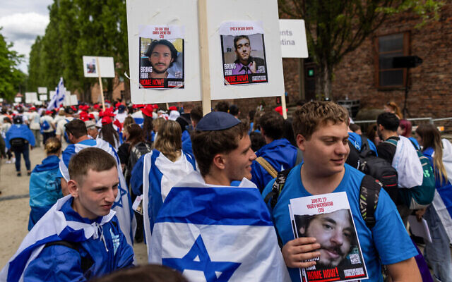 Des marcheurs portant des pancartes sur lesquelles on peut lire « Ramenez-le chez eux » ainsi que des photos d'otages des terroristes à Gaza lors de la Marche annuelle des vivants, en l'honneur des victimes de la Shoah, au mémorial et musée d'Auschwitz-Birkenau sur le site du camp de concentration d'Auschwitz, à Oswiecim, en Pologne, le 6 mai 2024. (Crédit : Wojtek Radwanski/AFP)