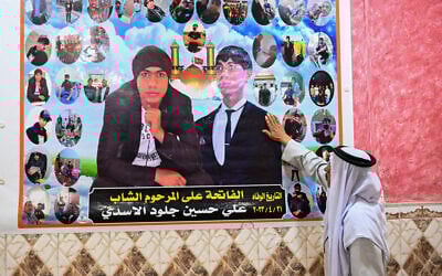 Hussein Joulood touchant un portrait de son fils décédé chez lui, en face du champ pétrolier de Rumaila, dans la province méridionale irakienne de Bassorah, le 5 mai 2024. (Crédit : Hussein Faleh/AFP)