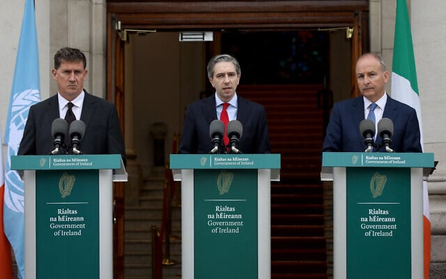 Le Premier ministre irlandais Simon Harris (au centre), entouré du ministre irlandais des Affaires étrangères Michel Martin (à droite) et du ministre des Transports Eamon Ryan (à gauche), annonçant la reconnaissance par son pays du statut d'État de Palestine, dans les bâtiments du gouvernement, à Dublin, en Irlande, le 22 mai 2024. (Crédit : Paul Faith/AFP) Le Premier ministre irlandais Simon Harris (au centre), entouré du ministre irlandais des Affaires étrangères Michel Martin (à droite) et du ministre des Transports Eamon Ryan (à gauche), annonçant la reconnaissance par son pays du statut d'État de Palestine, dans les bâtiments du gouvernement, à Dublin, en Irlande, le 22 mai 2024. (Crédit : Paul Faith/AFP)