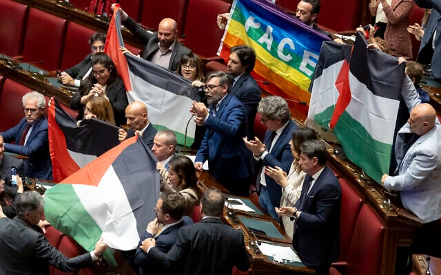 Plusieurs députés du Mouvement 5 étoiles, parti d'opposition italien, brandissent cinq drapeaux palestiniens et un drapeau de la paix à la Chambre basse des députés, le 28 mai 2024 au palais Montecitorio à Rome, lors d'une discussion sur la crise au Moyen-Orient, alors que leur collègue Riccardo Ricciardi prend la parole, appelant l'Italie à reconnaître l'État de Palestine. (Crédit : Massimo PERCOSSI / ANSA / AFP) Plusieurs députés du Mouvement 5 étoiles, parti d'opposition italien, brandissent cinq drapeaux palestiniens et un drapeau de la paix à la Chambre basse des députés, le 28 mai 2024 au palais Montecitorio à Rome, lors d'une discussion sur la crise au Moyen-Orient, alors que leur collègue Riccardo Ricciardi prend la parole, appelant l'Italie à reconnaître l'État de Palestine. (Crédit : Massimo PERCOSSI / ANSA / AFP)