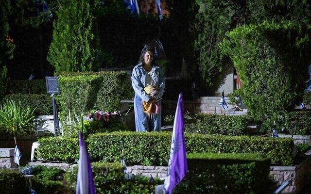 Une femme se tient debout en silence à côté des tombes des soldats israéliens tombés au combat au cimetière militaire du Mont Herzl à Jérusalem, alors qu'une sirène d'une minute retentit pour Yom HaZikaron, le 12 mai 2024. (Crédit : Yonatan Sindel/Flash90)