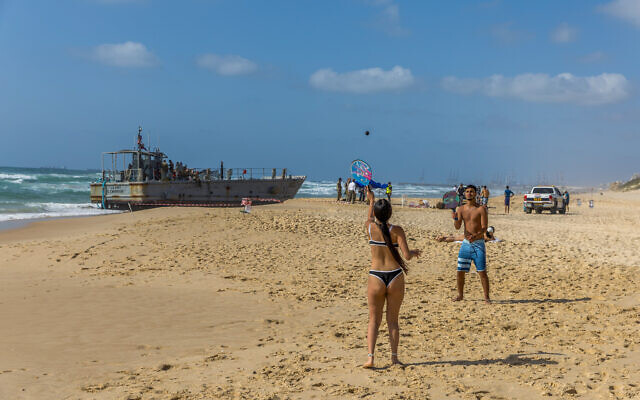 Des Israéliens près d'un navire de l'armée américaine échoué sur une plage d'Ashdod, le 25 mai 2024. (Crédit : Liron Moldovan/Flash90) Des Israéliens près d'un navire de l'armée américaine échoué sur une plage d'Ashdod, le 25 mai 2024. (Crédit : Liron Moldovan/Flash90)