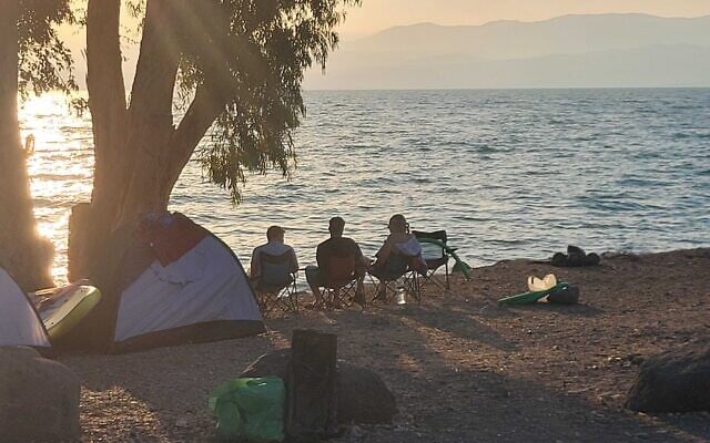 La famille Cohen d'Ashkelon regardant le coucher de soleil, sur le rivage de Gofra, au bord du lac de Tibériade, le 12 juin 2024. (Crédit : Canaan Lidor/Times of Israel)