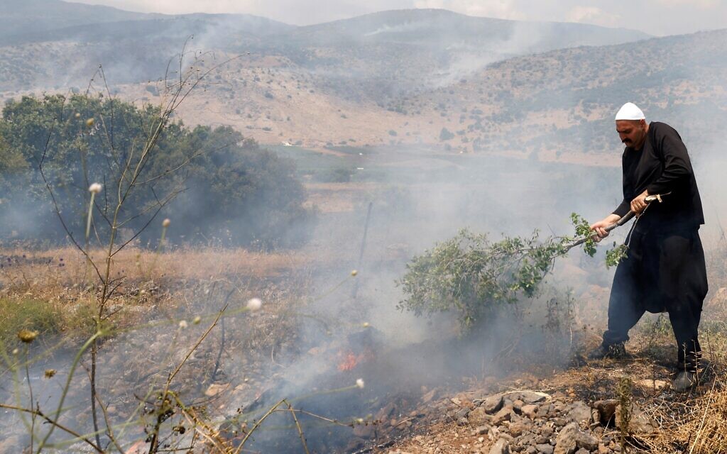 Un Druze tente d'éteindre un début d'incendie dans un champ après que que des roquettes lancées depuis le sud du Liban sont retombées dans le secteur de Banias, sur le plateau du Golan, le 9 juin 2024. (Crédit : Jalaa MAREY / AFP)