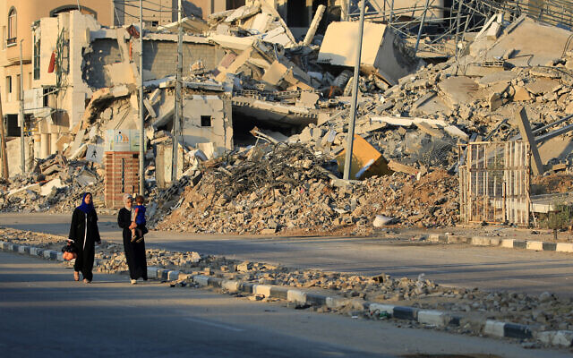 Des Palestiniens déplacés passent devant des bâtiments détruits dans le camp de réfugiés d'al-Bureij, dans le centre de la bande de Gaza, le 12 juin 2024. (Crédit : Eyad BABA / AFP)